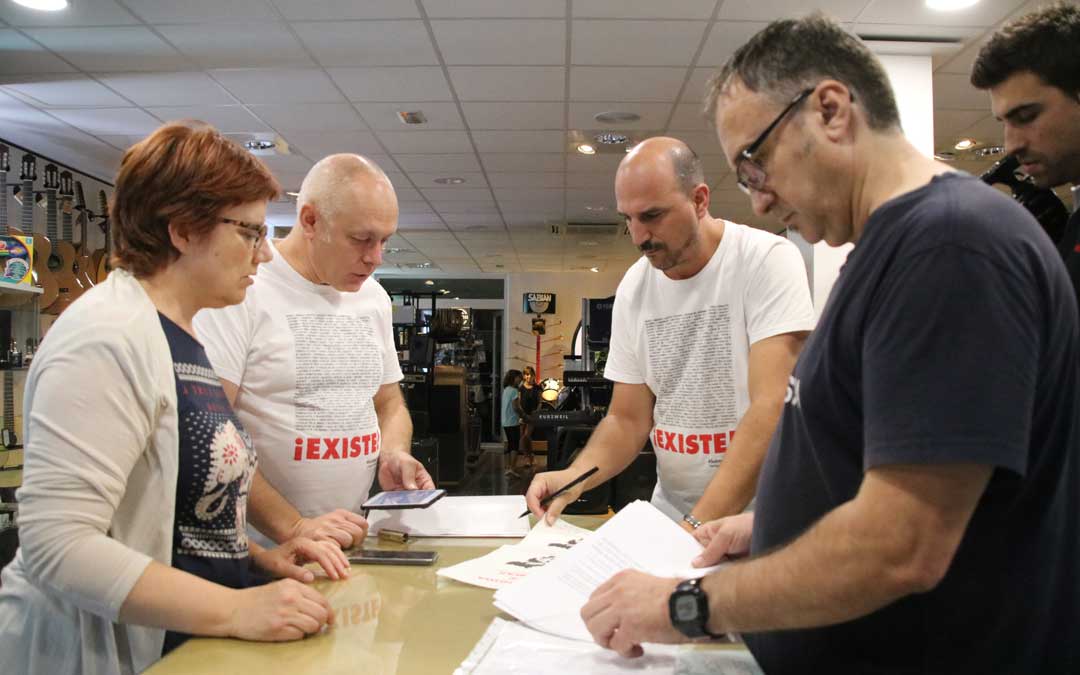 Tres miembros de Teruel Existe Bajo Aragón Mª Ángeles Lahoz, Toño Saz y Joaquín Egea; este jueves, con las hojas de firmas que se encuentran en 44600 Música de Alcañiz junto a su propietario, Carlos Gargallo. / A. Monserrate