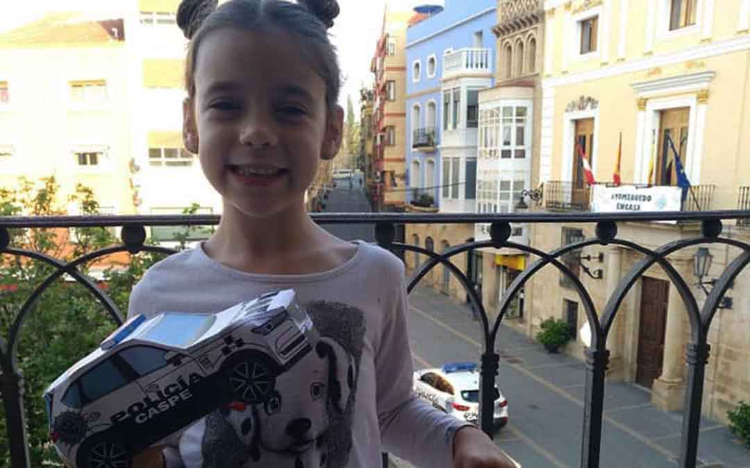 Niña con su coche de Policía Local de Caspe hecho de papel.