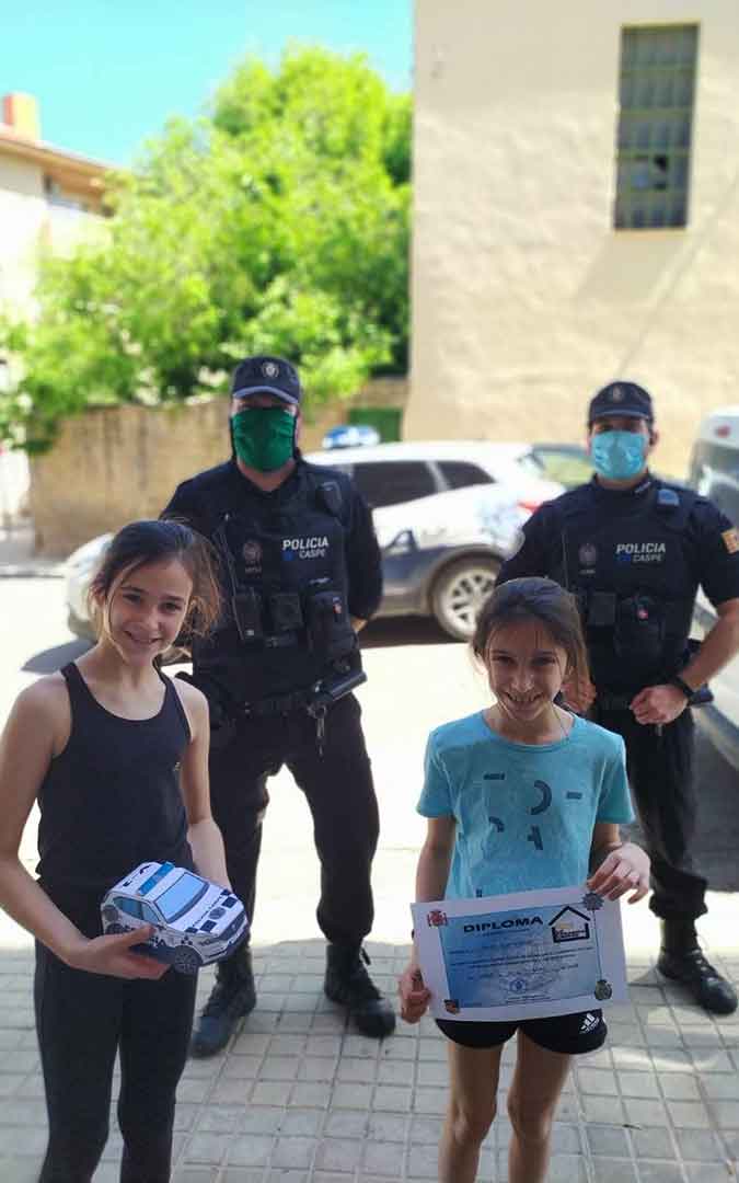 Dos niños con sus coches hechos de papel junto a dos policías locales en Caspe.