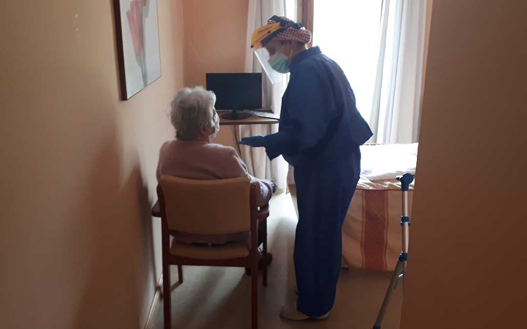 Una de las trabajadoras de la residencia de Valderrobres equipada con un traje de máxima protección atendiendo a una anciana en su habitación en el centro