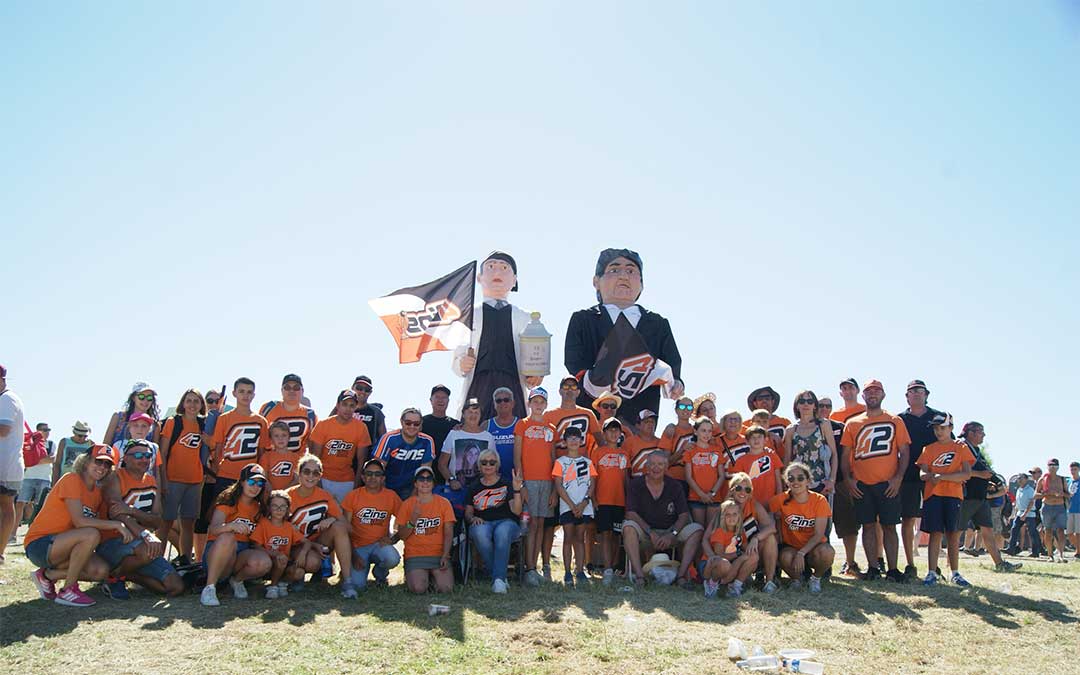 Una parte de la Asociación de Amigos de Álex Rins en 2018 en la pelouse 6, su zona de acción desde la que animan con sus dulzainas y banderas y custodiados por los gigantes del boticario Sastrón y el catedrático Casanova./ L.C.