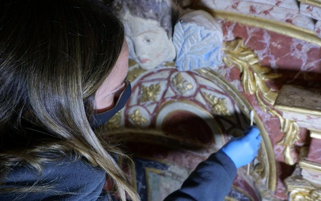 Una restauradora rescata los colores originales de un ángel en la parte superior del retablo./Heraldo