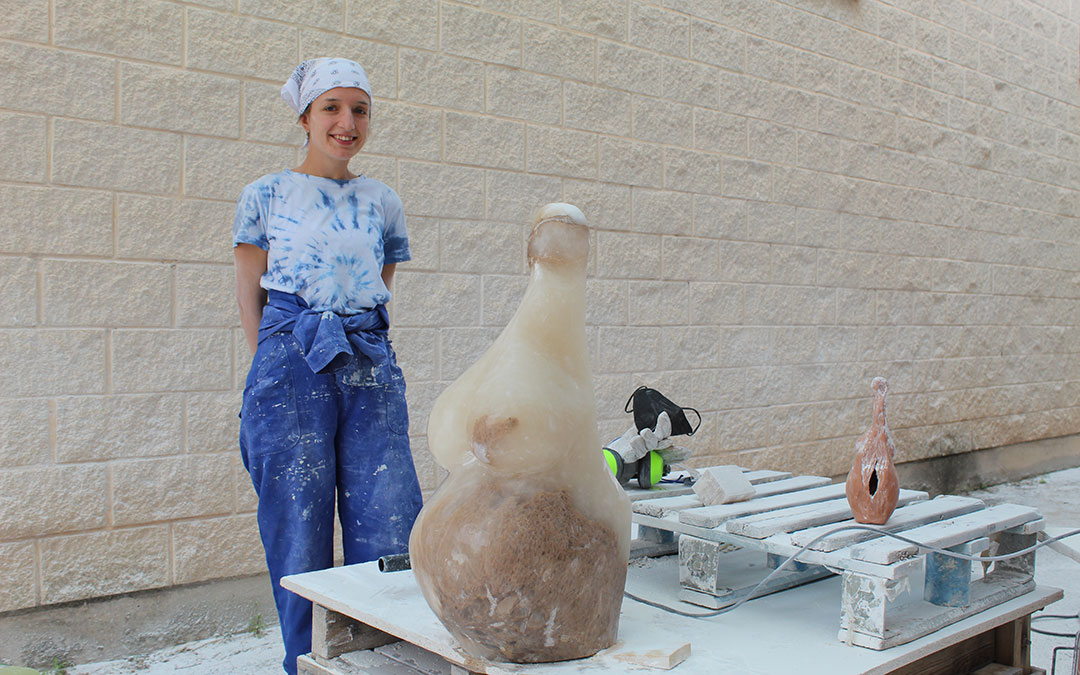 Estela Ferrer, en la recta final de perfilado de la escultura que representa a una mujer embarazada y en la que ya se ven los colores que escondía el bolo. Al lado, la parte trasera del boceto sobre el que se basó. / B. SEVERINO