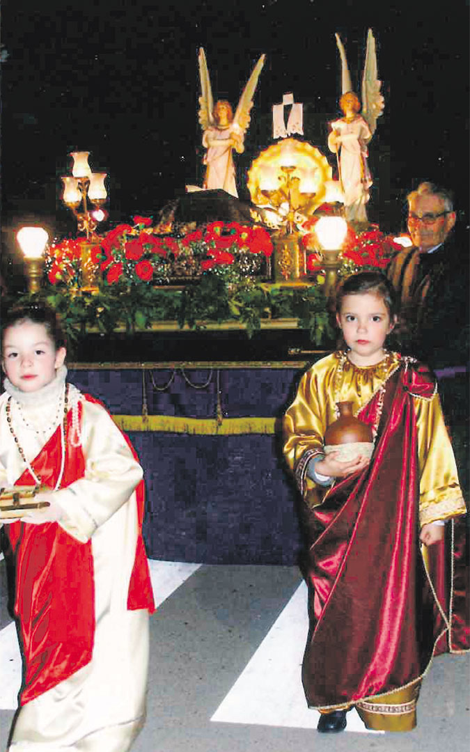 Alicia Martín de niña avanza de hebrea delante de su abuelo Jesús y junto a su amiga Pilar Garín Pina, de la familia propietaria del paso del Cristo Yacente. / Archivo familia Martín