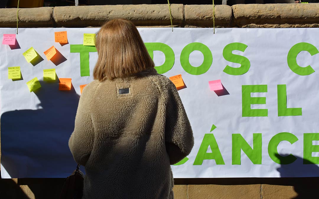 Una vecina frente a la pancarta de 'Todos unidos contra el cáncer', que se elaboró con motivo del Día Mundial Contra el Cáncer en Alcañiz./ A.M.