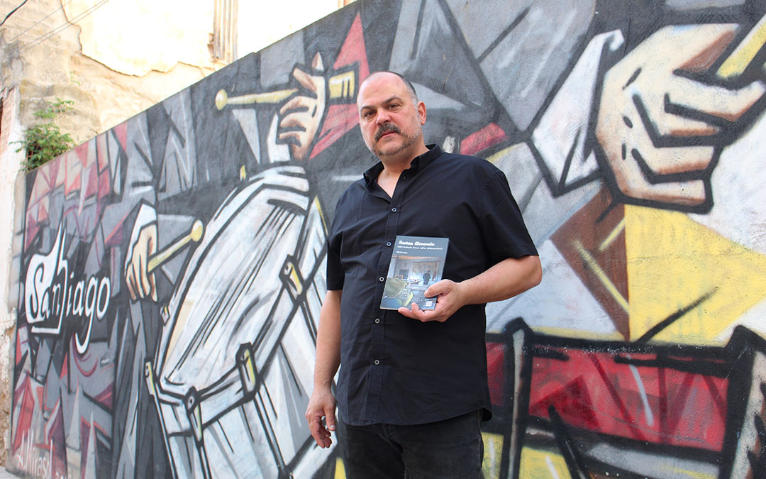 Víctor Guiu ante el mural de Álex Mirasol en la tapia del bar Santiago, donde suele realizar sus presentaciones y las de amigos en Híjar. / B. Severino