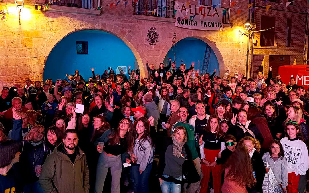 Vecinos de Alloza durante las fiestas. De fondo, el cartel de 'Alloza Bonica Pa’cutio' (Bonica para siempre)./ Comisión.