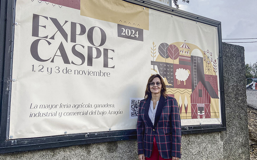 Ana Jarque junto al cartel promocional de Expo Caspe, que preside la entrada del pueblo. / A.Z