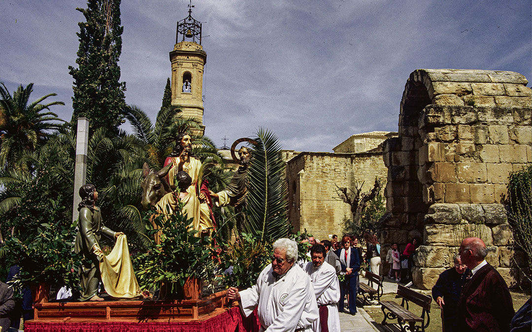 La imagen de La Burreta procesionando el Domingo de Ramos con La Colegiata de fondo./ La Burreta