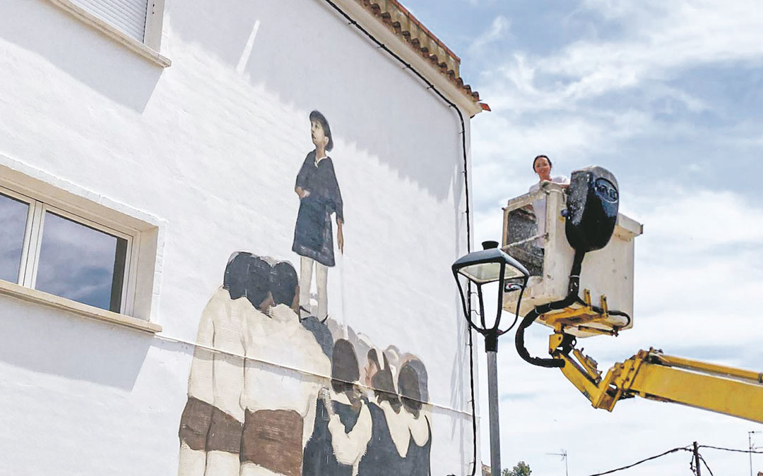 Yasmina Oliveros junto al mural de la escena central de La Rueda en una de las fachadas de la Casa de Cultura. / Ayto. Urrea