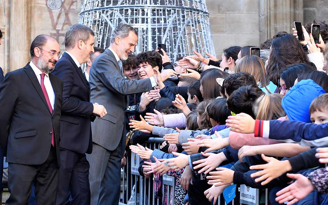 Javier Lambán, en primer término, sonríe mientras el Rey Felipe VI saluda a los más jóvenes en su visita a Alcañiz en diciembre de 2022 siendo él presidente de Aragón. Entre ambos, Ignacio Urquizu, entonces alcalde. / La Comarca