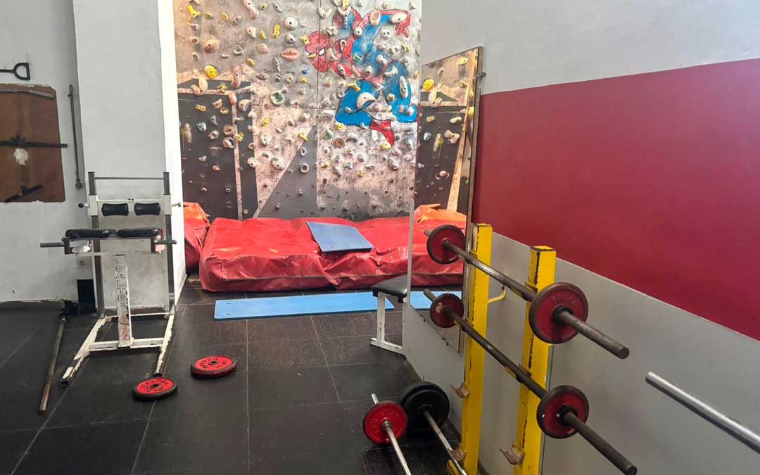 Parte de la zona de musculación del gimnasio con aparatos oxidados. De fondo, el rocódromo recién arreglado. / L.C.