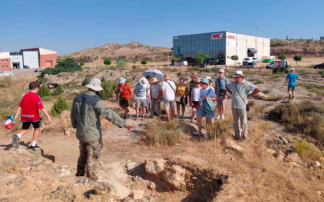 Los visitantes, ataviados con gorros y sombrillas para combatir el calor, prestan atención a las explicaciones sobre el yacimiento / Francisco Castro