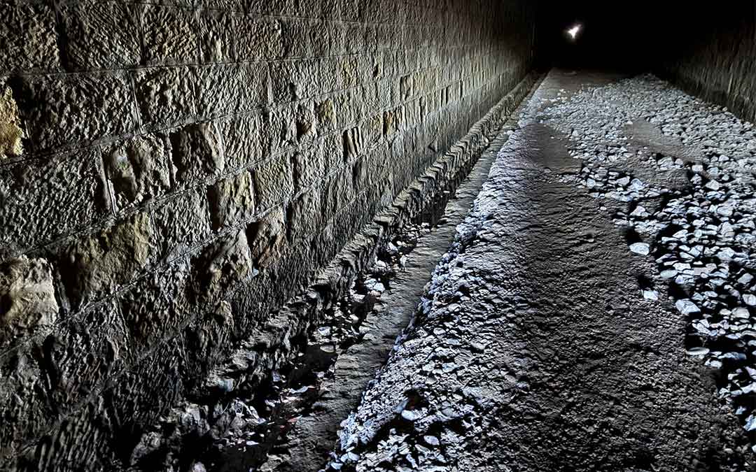 En el interior del túnel del Equinoccio se acumulan numerosas piedras de balastro que iban a sustituir por riego asfáltico pero se quedó a medias, lo que hace el paso intransitable. / Andrés Giner